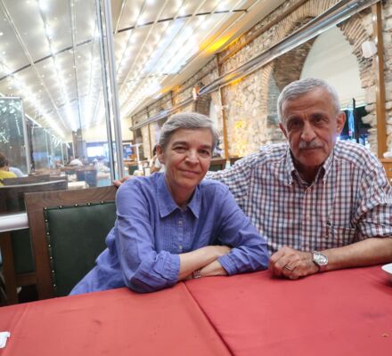 Christina und Necati an einem Restauranttisch mit rotem Tischtuch und Mauer im Hintergrund