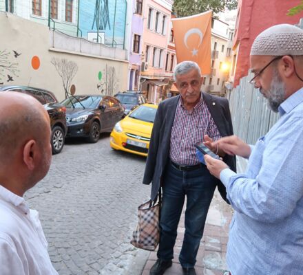 Necati mit zwei Freunden beim Plaudern auf der Strasse. Im Hintergrund türkische Fahne und gelbes Taxi.