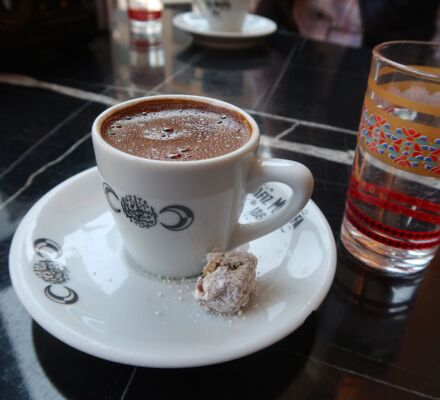 eine weisse Tasse türkischer Kaffee auf schwarzem Marmortisch mit Wasserglas mit buntem Dekor
